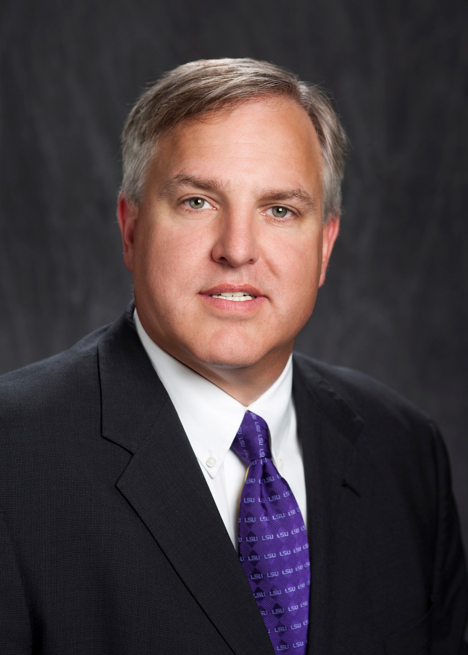 Ray Castle wearing a black suit, white shirt, and a purple tie.